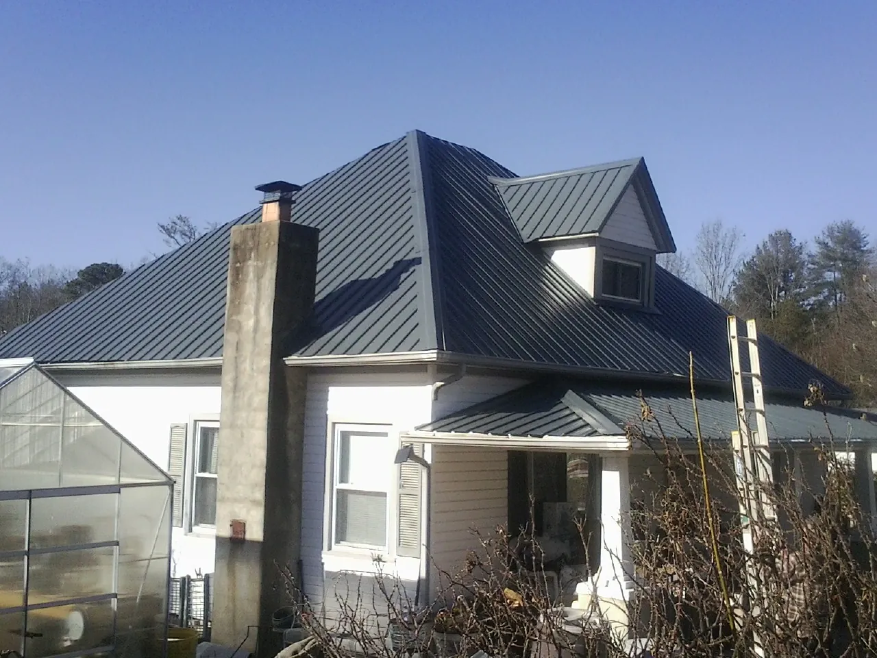 Dark blue standing seam metal roof on a white farmhouse with dormer — Slate & Tile Roof Repair by Roofing Brothers in Remsen