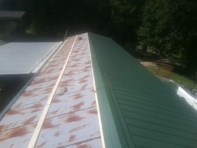 Old rusted panels beside newly installed green metal roofing — Wind Damage Roof Repair by Roofing Brothers in Remsen