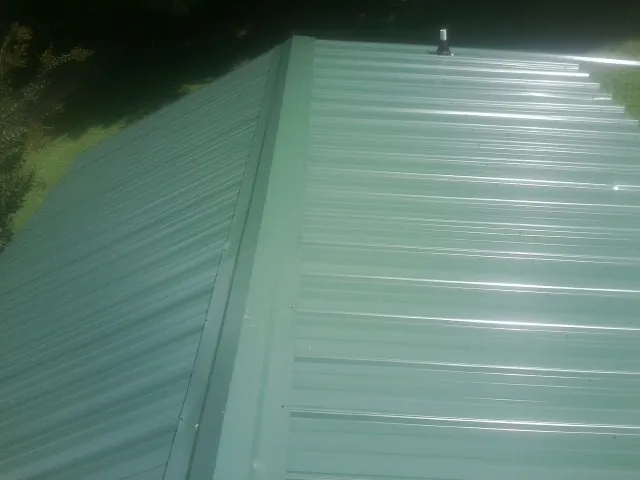 New green metal panels meeting at the ridge of a roof — Flat Roof Repair work by our crew in Remsen