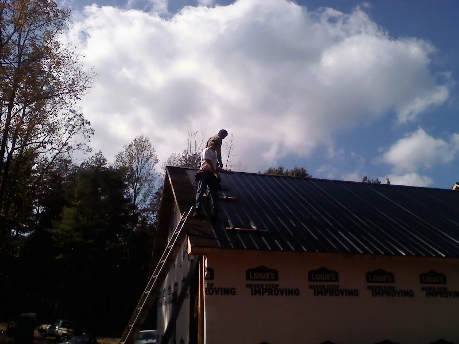Roofer fastening dark metal panels high against a cloudy sky, from a Roof Inspection job in Remsen