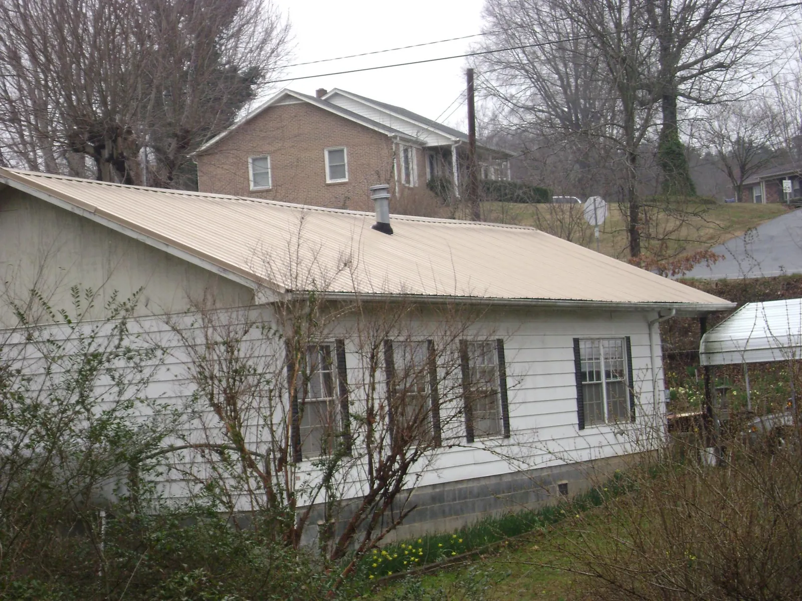 Tan metal roof on a white sided house set into a hillside — Commercial Roofing by Roofing Brothers in Remsen