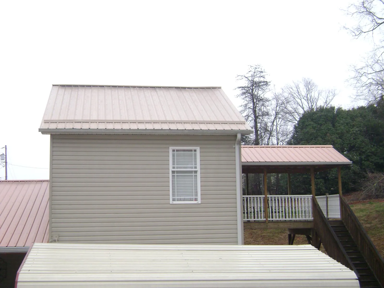 Tan metal roofs on a two story addition and attached porch, from a Roof Replacement job in Remsen