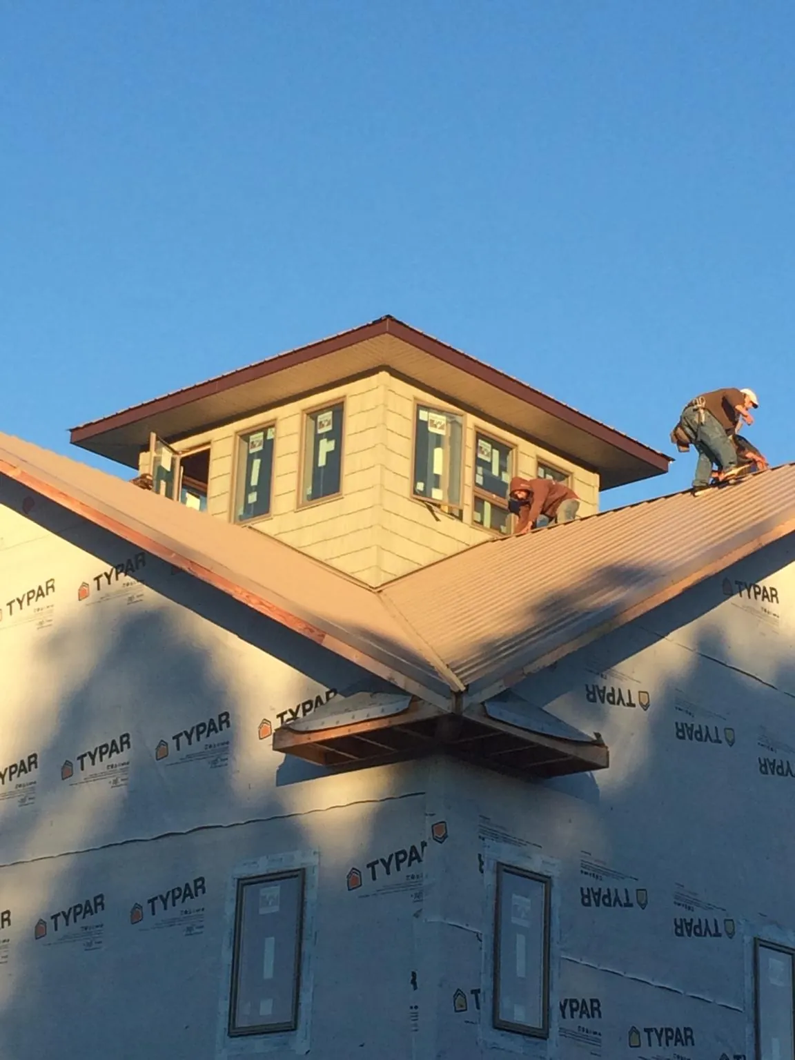 Roofers working around a rooftop cupola on a new metal roof at sunset — Roof Waterproofing in Remsen by Roofing Brothers